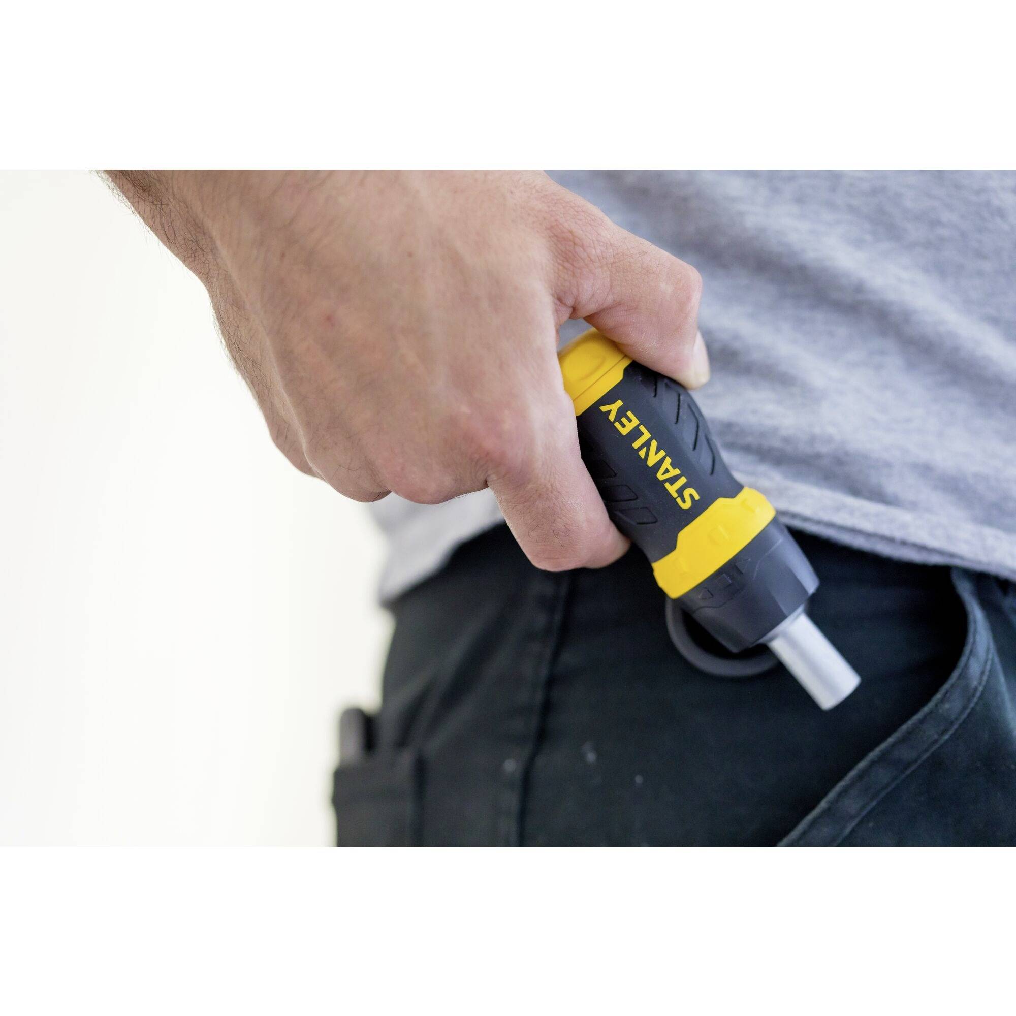 Une main tient un tournevis électrique jaune et noir de STANLEY près d'un pantalon noir.