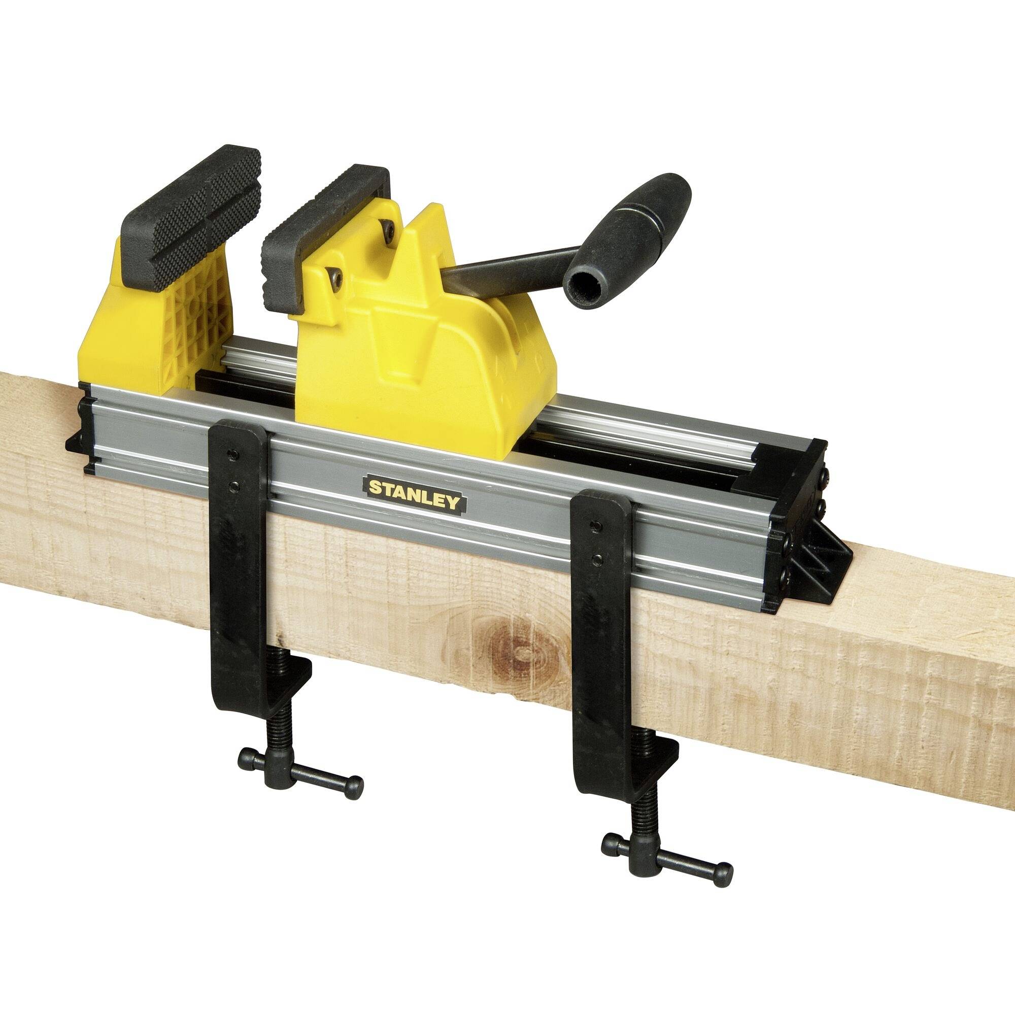 Un morceau de bois est maintenu par un étau jaune sur un établi. L'étau est fixé avec deux pinces noires.