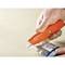 Une main utilise un coupe-carton orange pour ouvrir un sac en plastique contenant des vis. Un tableau est visible en arrière-plan.