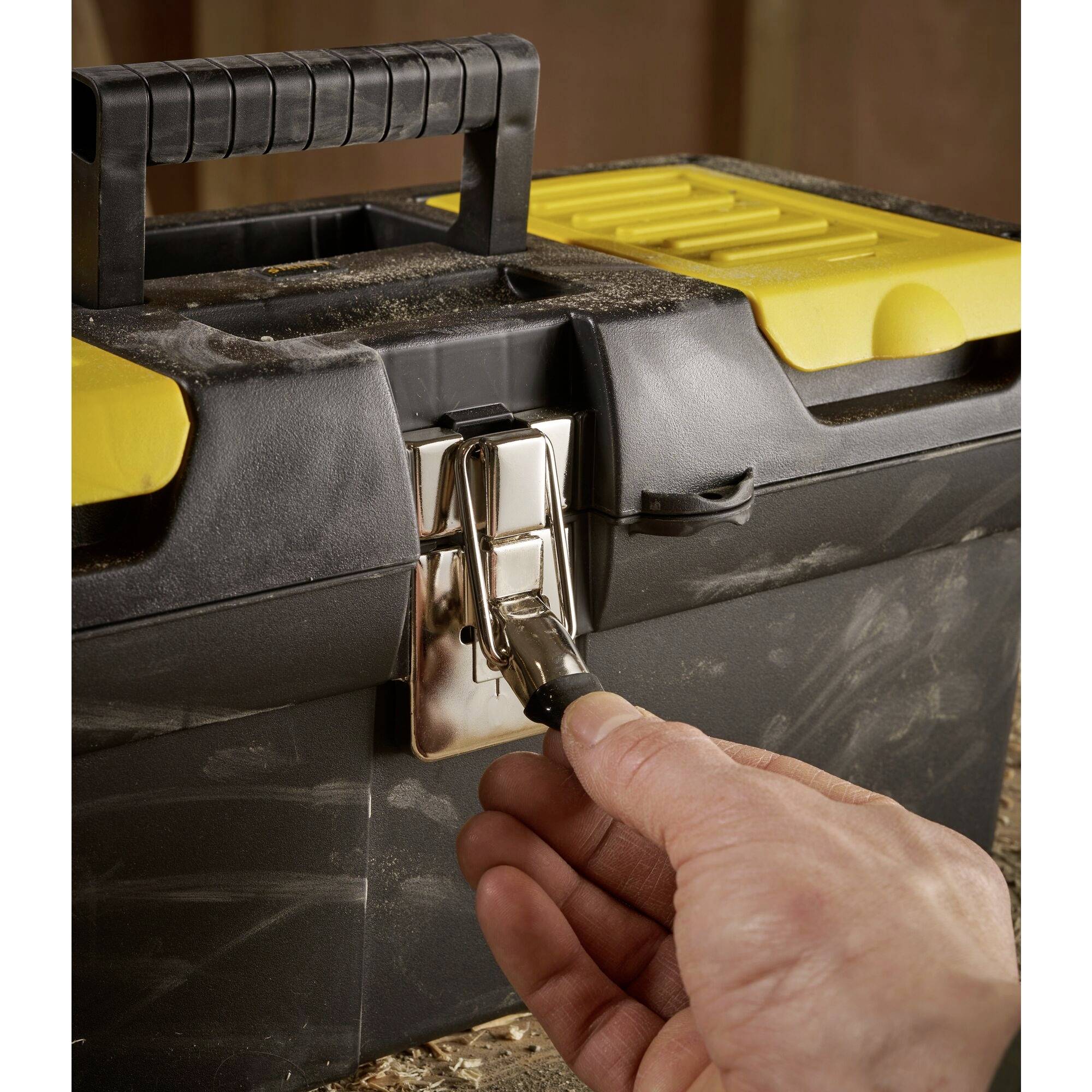 Une main ouvre le verrou d'une grande boîte à outils noir et jaune avec une poignée.