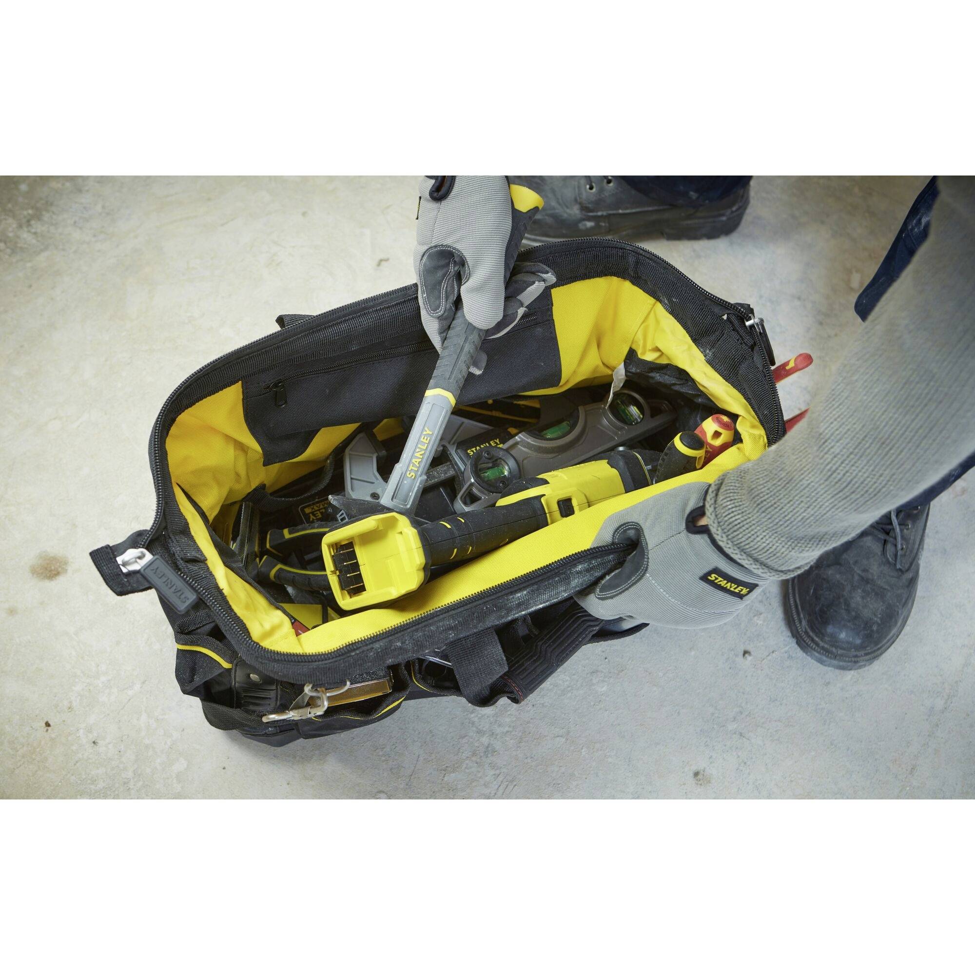 Un sac à outils ouvert, rempli de différents outils tels que des clés et des pinces. Une personne tend la main vers un outil.