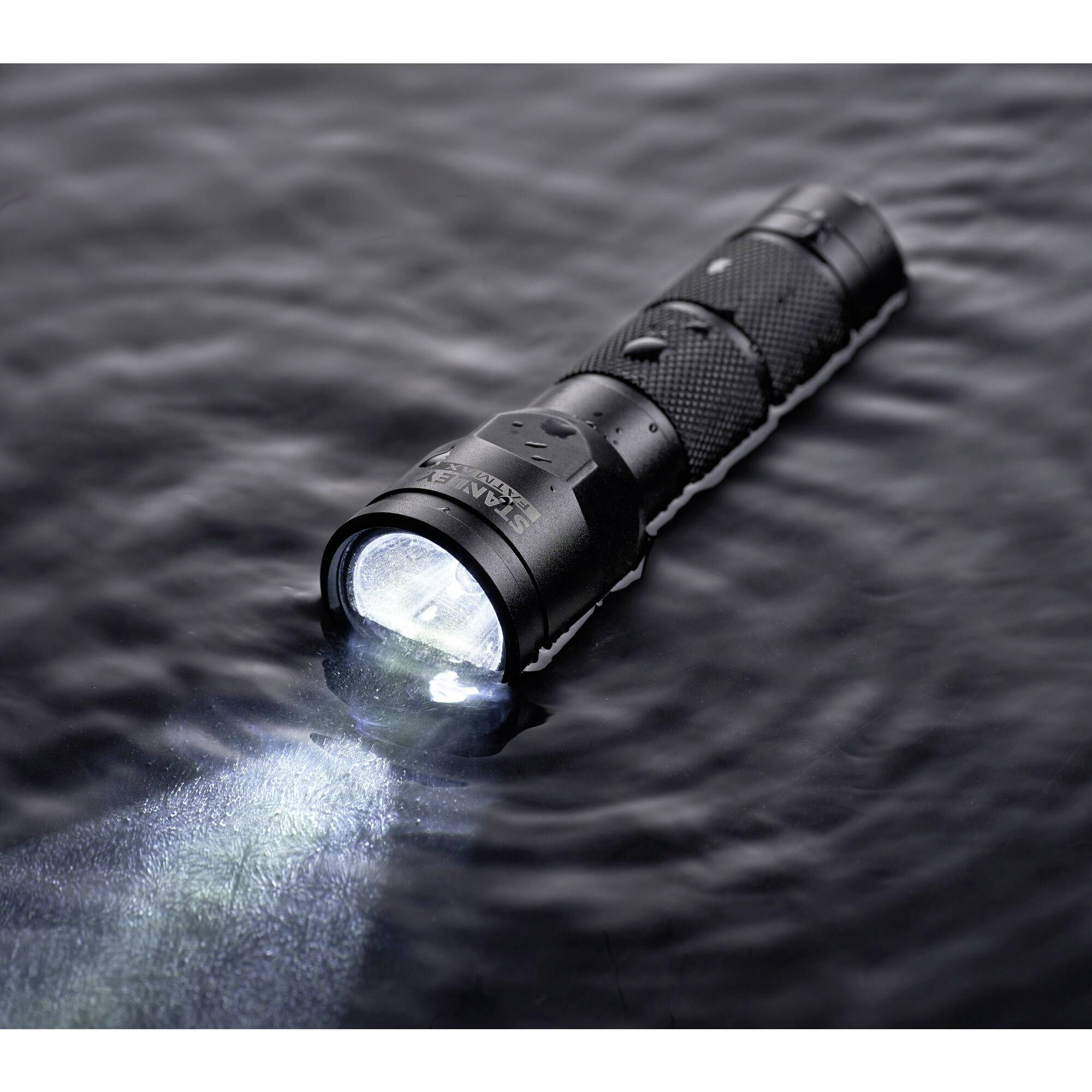 Une lampe de poche étanche flotte et brille à la surface d'un plan d'eau sombre.
