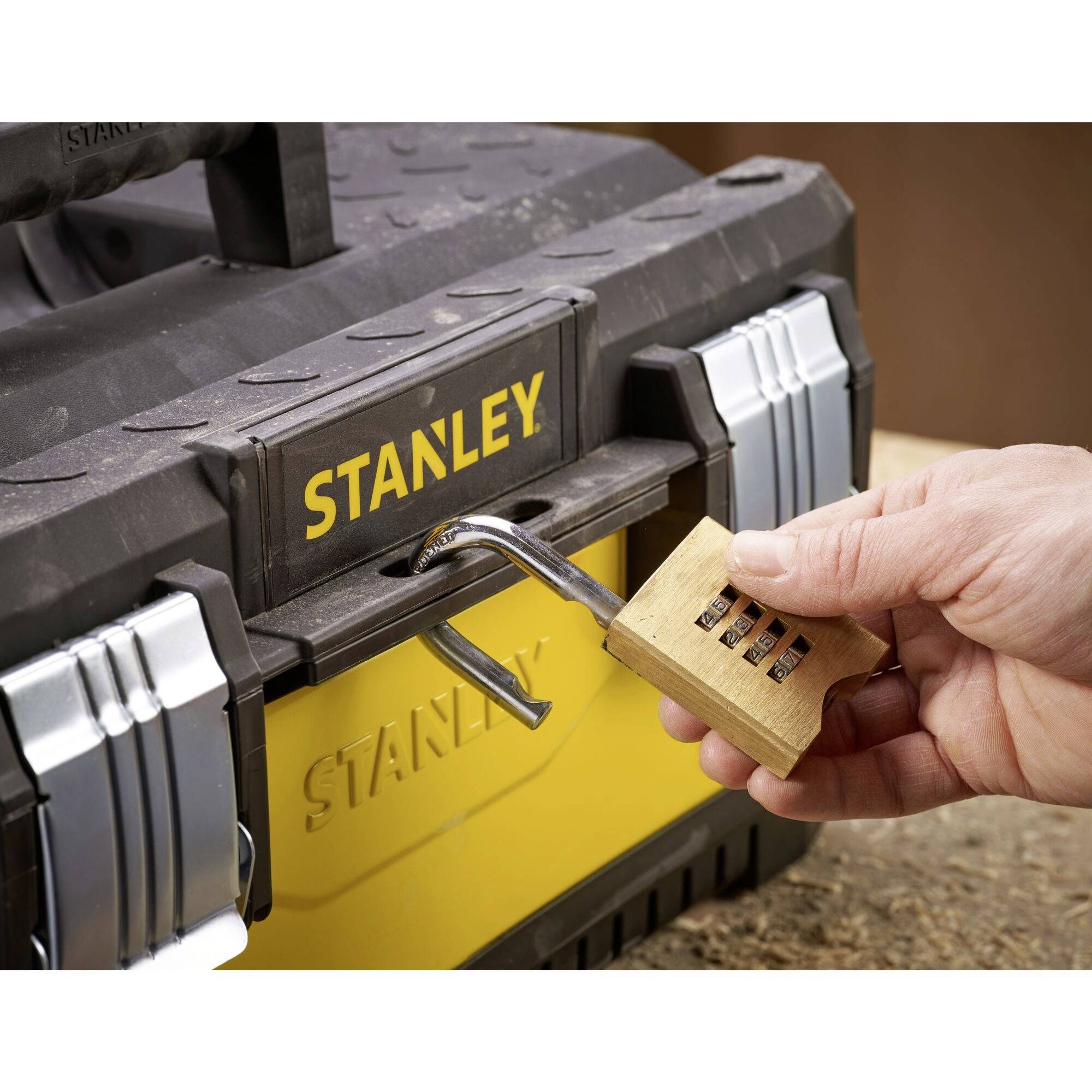 Une main ferme un cadenas à code sur une boîte à outils noire avec un imprimé jaune.