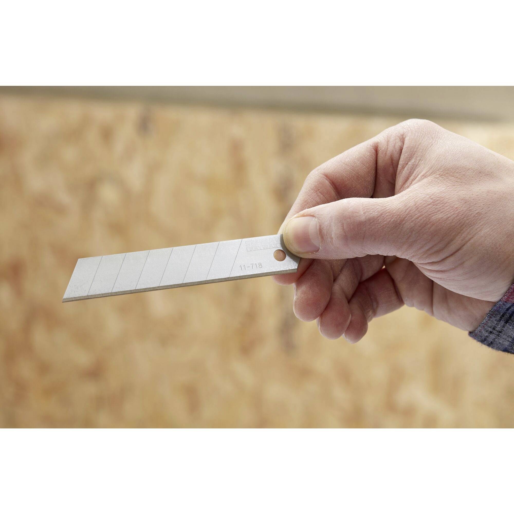 Une main tient un couteau à lame rétractable argenté devant un arrière-plan flou de texture en bois.