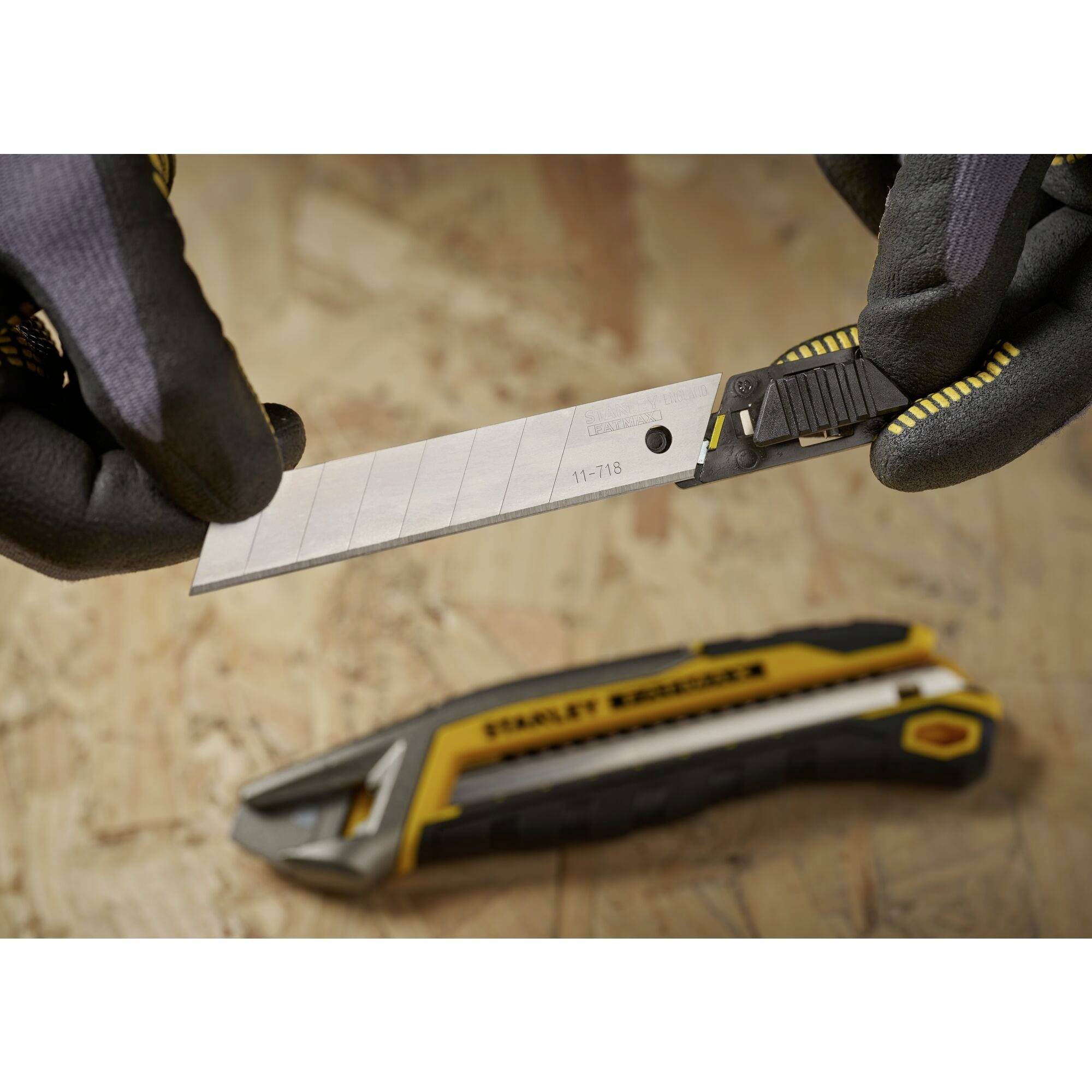 Une personne tient un cutter alors qu'un autre cutter est posé sur une table en bois. Les deux couteaux sont noir et jaune.