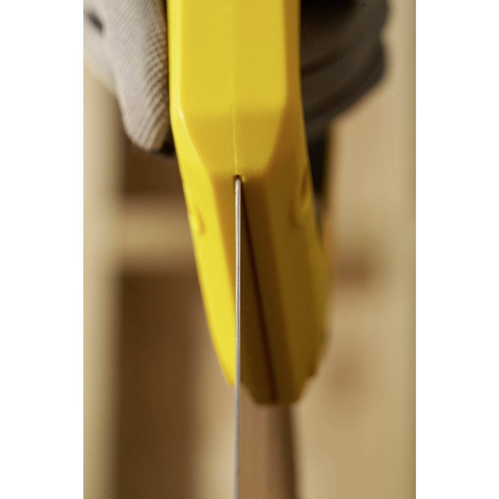 Gros plan d'une scie à main jaune utilisée par une personne pour couper un morceau de bois. La main porte un gant de sécurité.