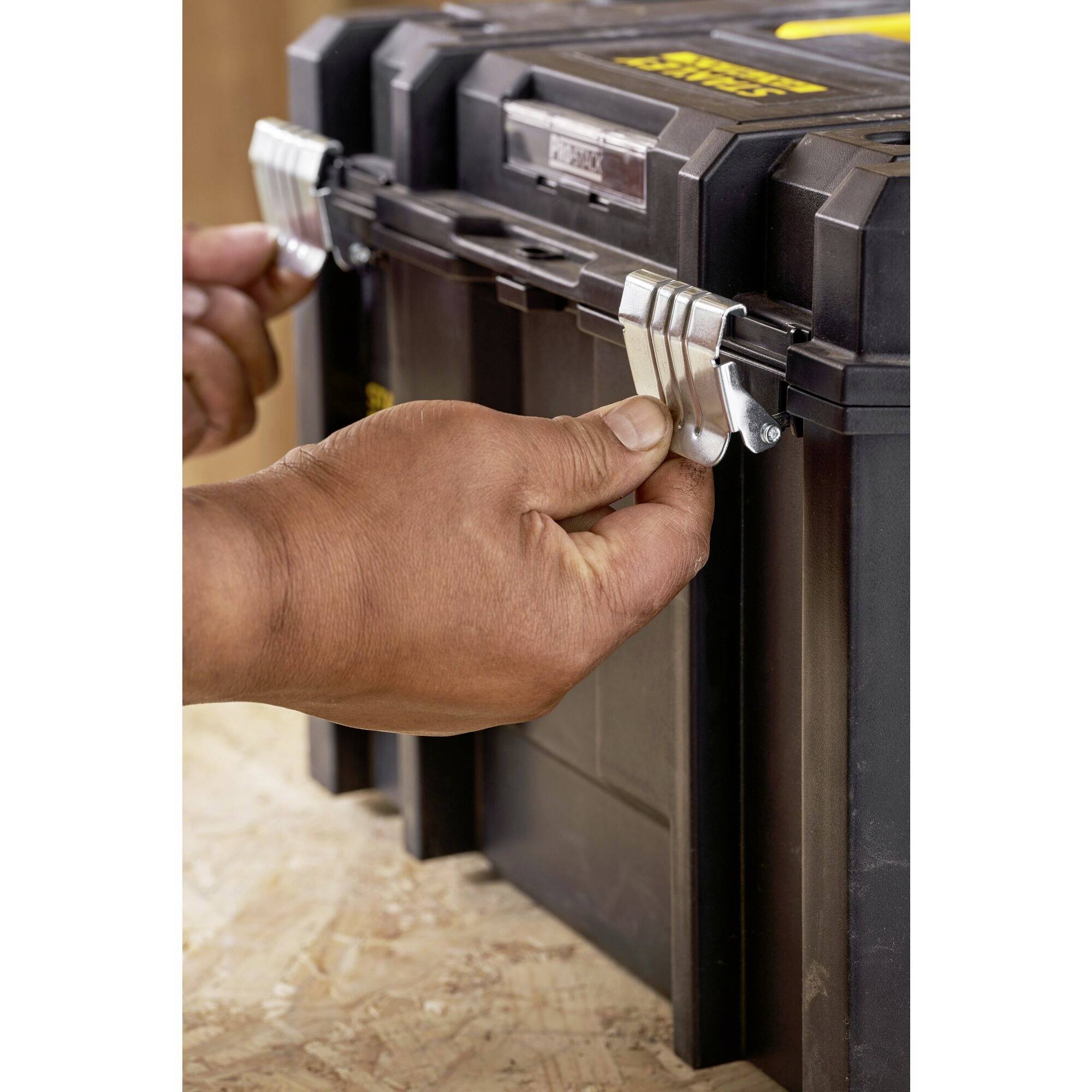 Une personne déverrouille une boîte à outils noire avec des fermoirs métalliques sur une table en bois.
