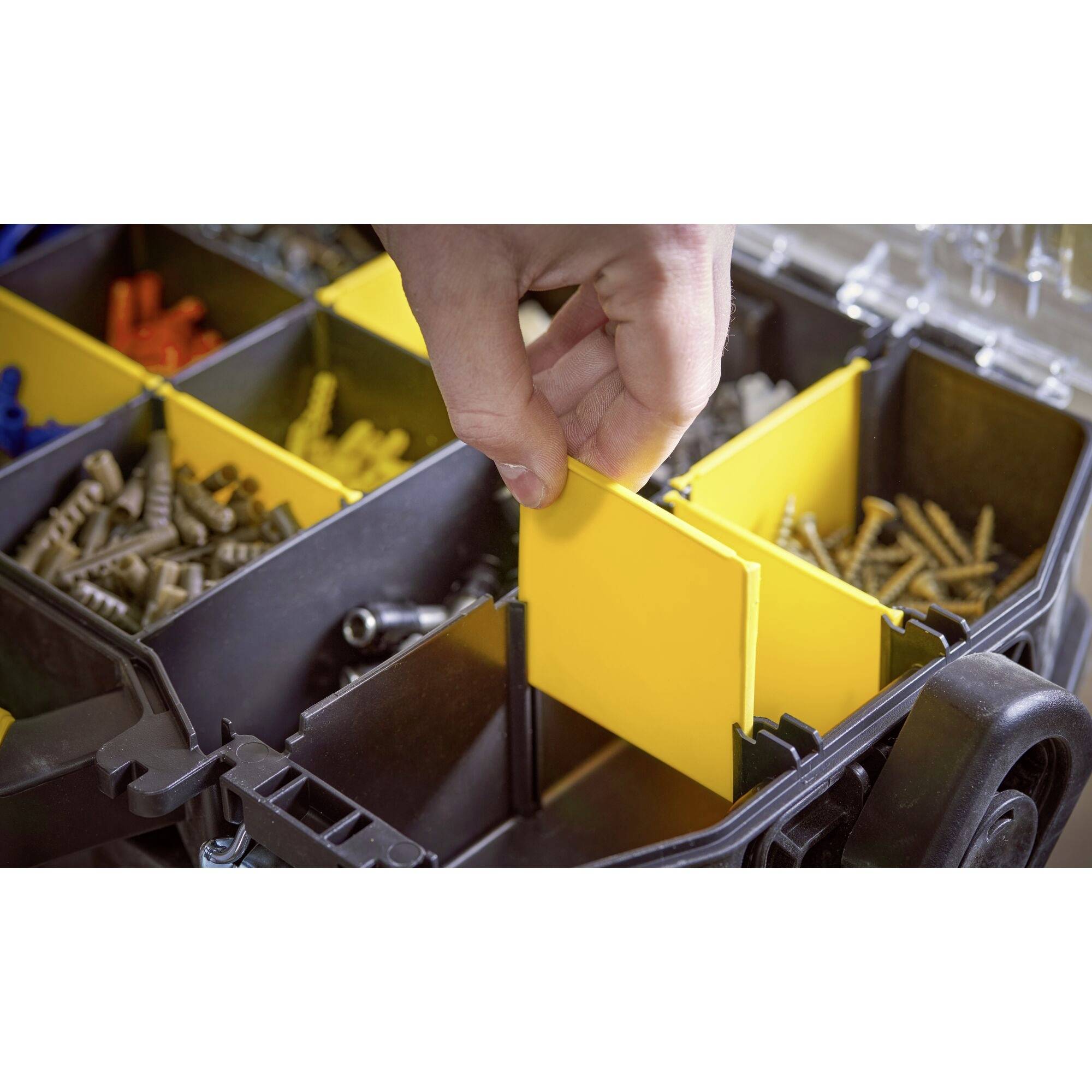 Une main saisit une cloison jaune dans une boîte de tri remplie de vis et de chevilles.