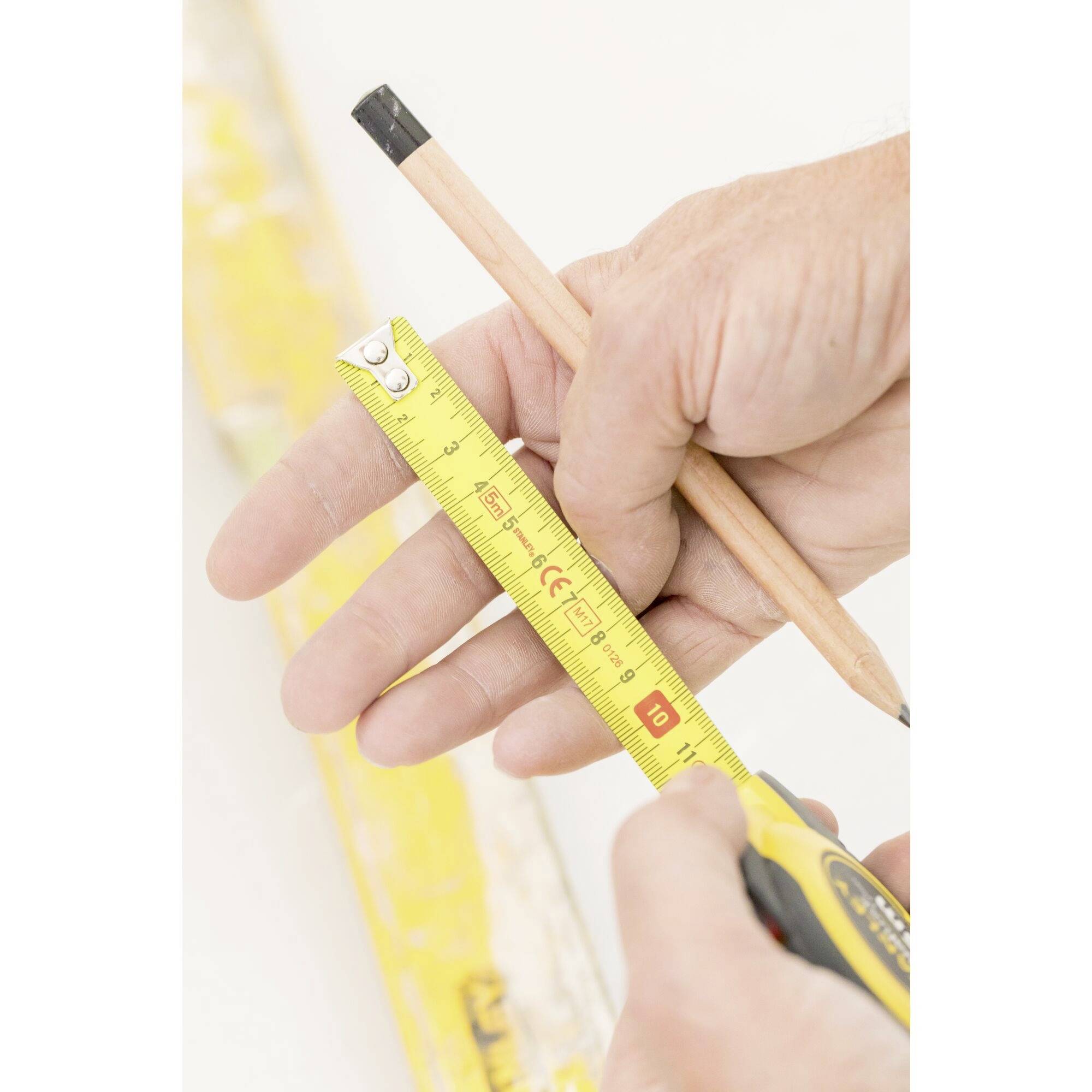 Une personne tient un ruban à mesurer jaune et un crayon à la main, prête à mesurer ou à marquer sur une surface.