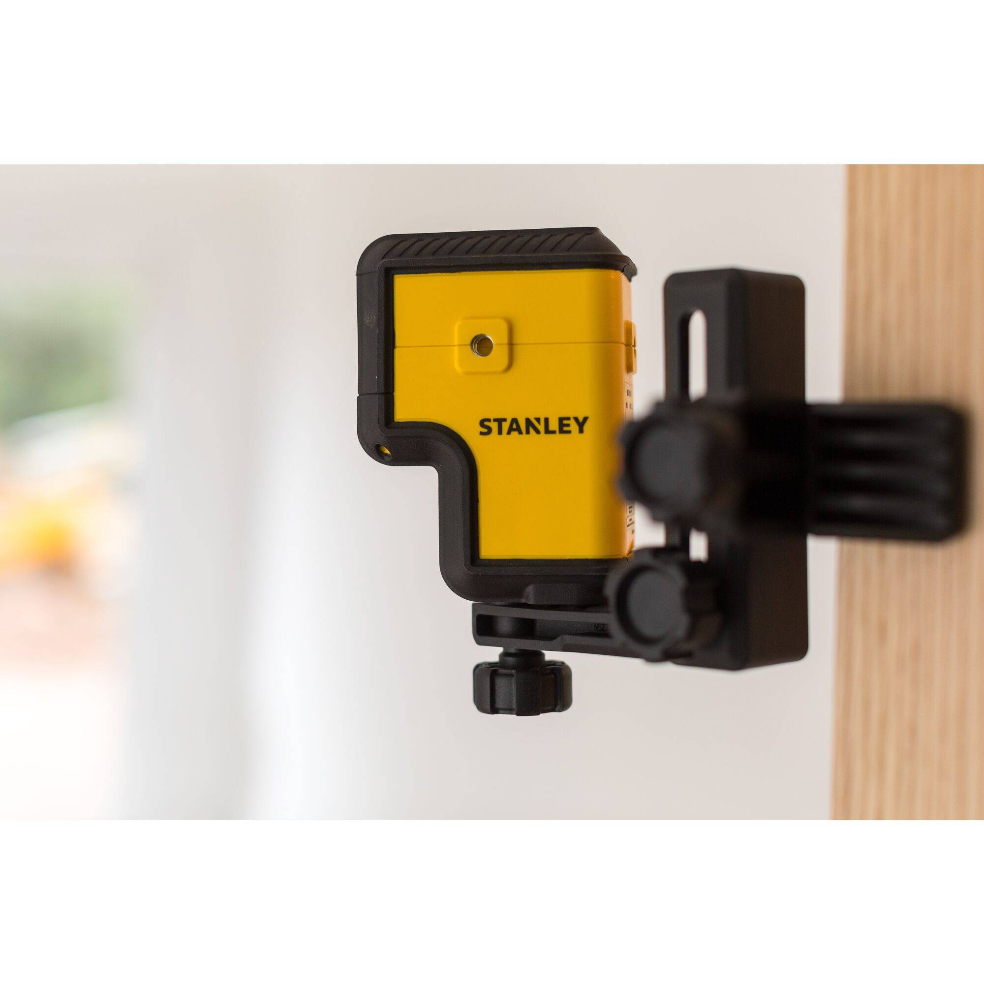 Un appareil de nivellement laser jaune avec un boîtier noir est fixé à une surface en bois et prêt pour des travaux de construction.