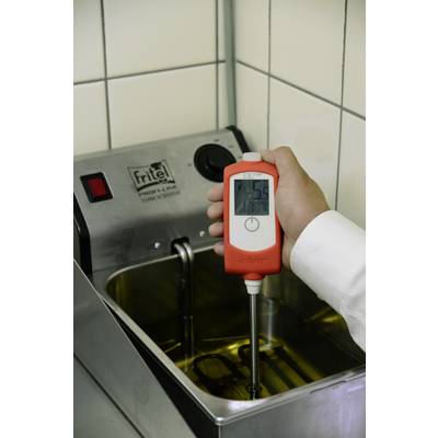 Une personne tient un thermomètre au-dessus d'une friteuse et mesure la température de l'huile. L'écran affiche 75,6 degrés.