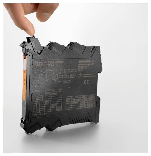 La main d'une personne ajuste ou tient un module électronique compact noir avec un étiquetage détaillé, vraisemblablement utilisé pour des systèmes industriels.