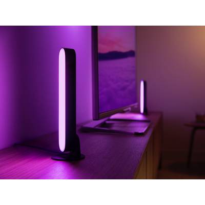Deux lampes LED verticales émettant une lumière violette, placées de part et d'autre d'un écran sur un bureau dans une pièce obscure.