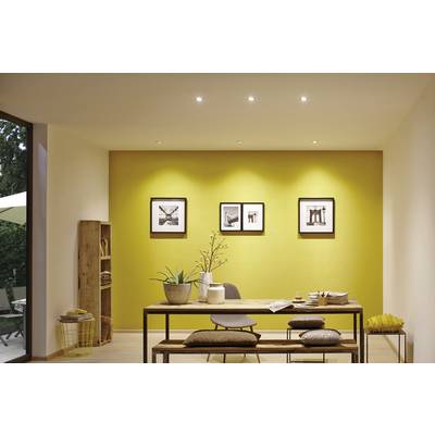 Salle à manger avec un mur jaune, une table en bois et quatre chaises. Derrière la table, trois photos encadrées en noir et blanc sont suspendues.