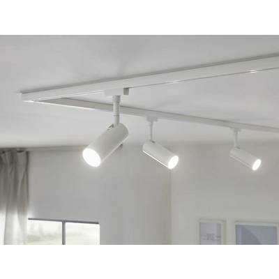 Trois projecteurs LED plafonniers lumineux sur une rails, éclairent une pièce. Un rideau gris et une fenêtre sont visibles en arrière-plan.