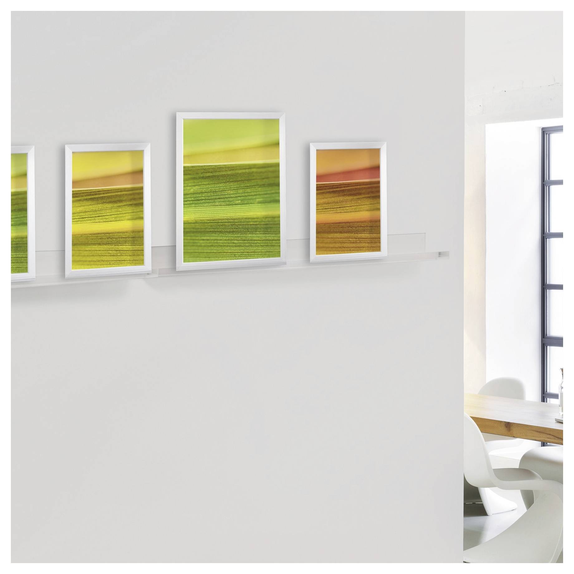 Un mur galerie minimaliste avec quatre impressions de paysages abstraits encadrées en jaune, vert et orange, à côté d'une zone de repas lumineuse.