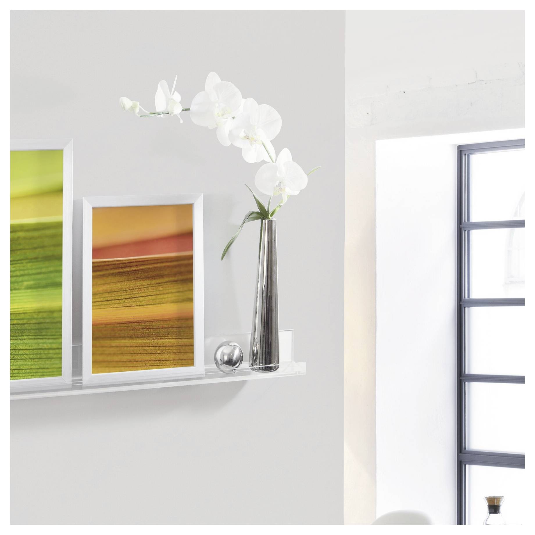 Étagère murale minimaliste avec cadre d'art abstrait, un vase argenté contenant des orchidées blanches, et une grande fenêtre ou miroir sur la droite.