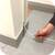« Une pièce au sol carrelé. Une personne fait passer un fil transparent à travers un petit interstice entre les carreaux du sol et le mur. »