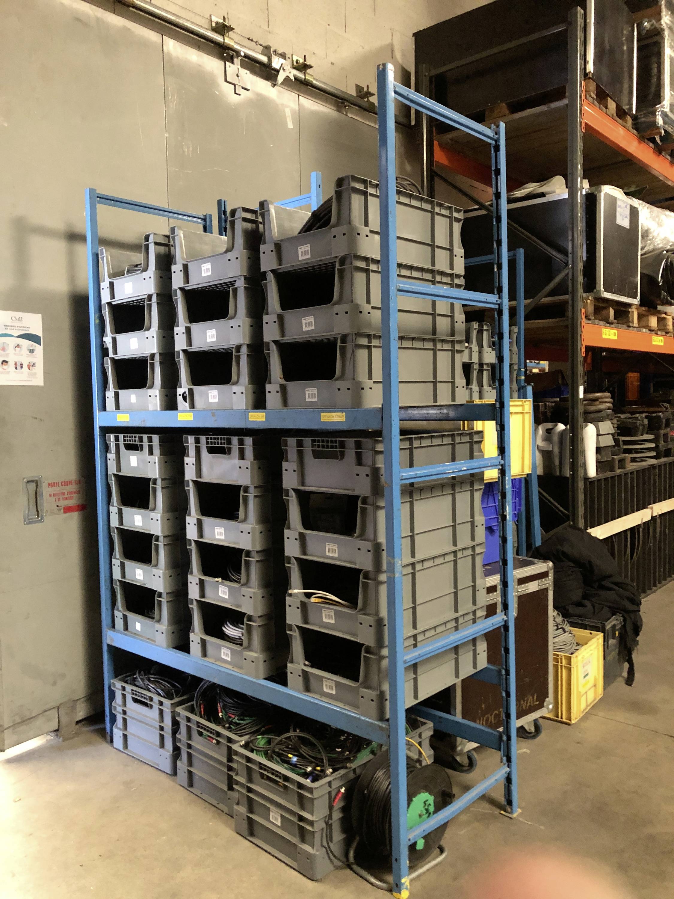 Étagère avec des caisses en plastique gris empilables dans un local de stockage, remplies de divers équipements.