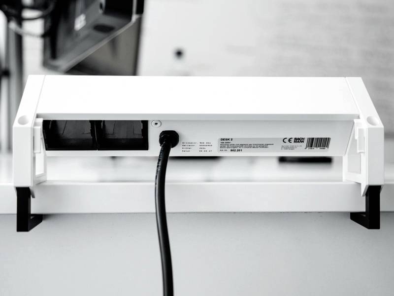Un appareil électrique blanc avec des prises et un cordon d'alimentation est posé sur une table. Il est connecté et fixé sous un bureau.