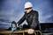 Un homme portant un casque et des lunettes de protection travaille sur un chantier, tient un outil électrique et se penche sur des barres d'acier.
