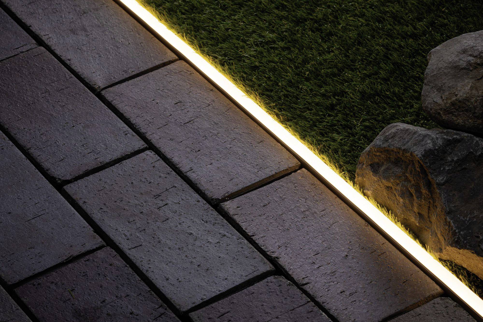 L'éclairage de jardin présente une bande LED chaleureusement illuminée entre les dalles de terrasse et le gazon synthétique ; créant une atmosphère intimiste.