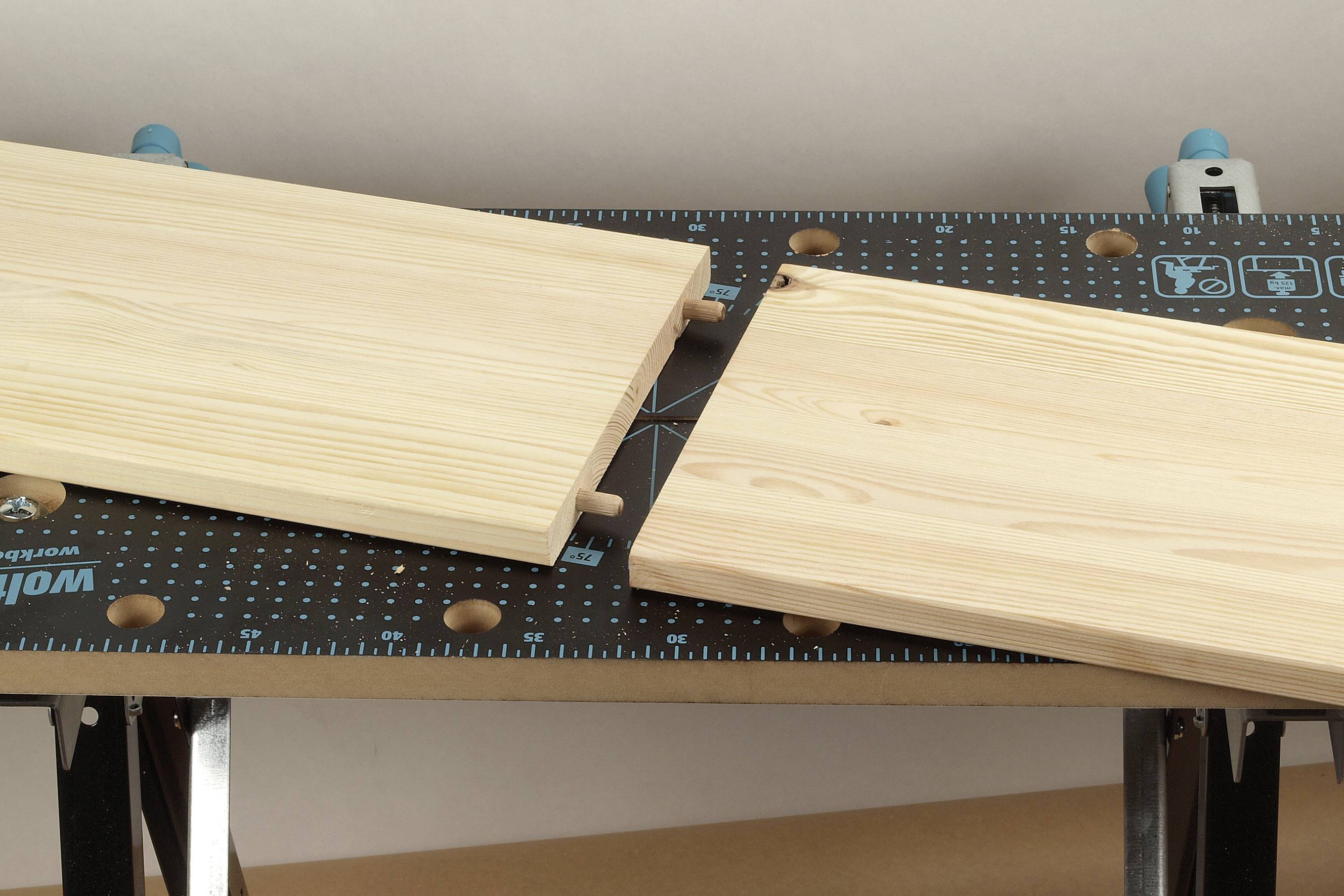 Deux planches de bois sur un établi, reliées par des chevilles en bois selon la technique d'assemblage à tenon et mortaise.