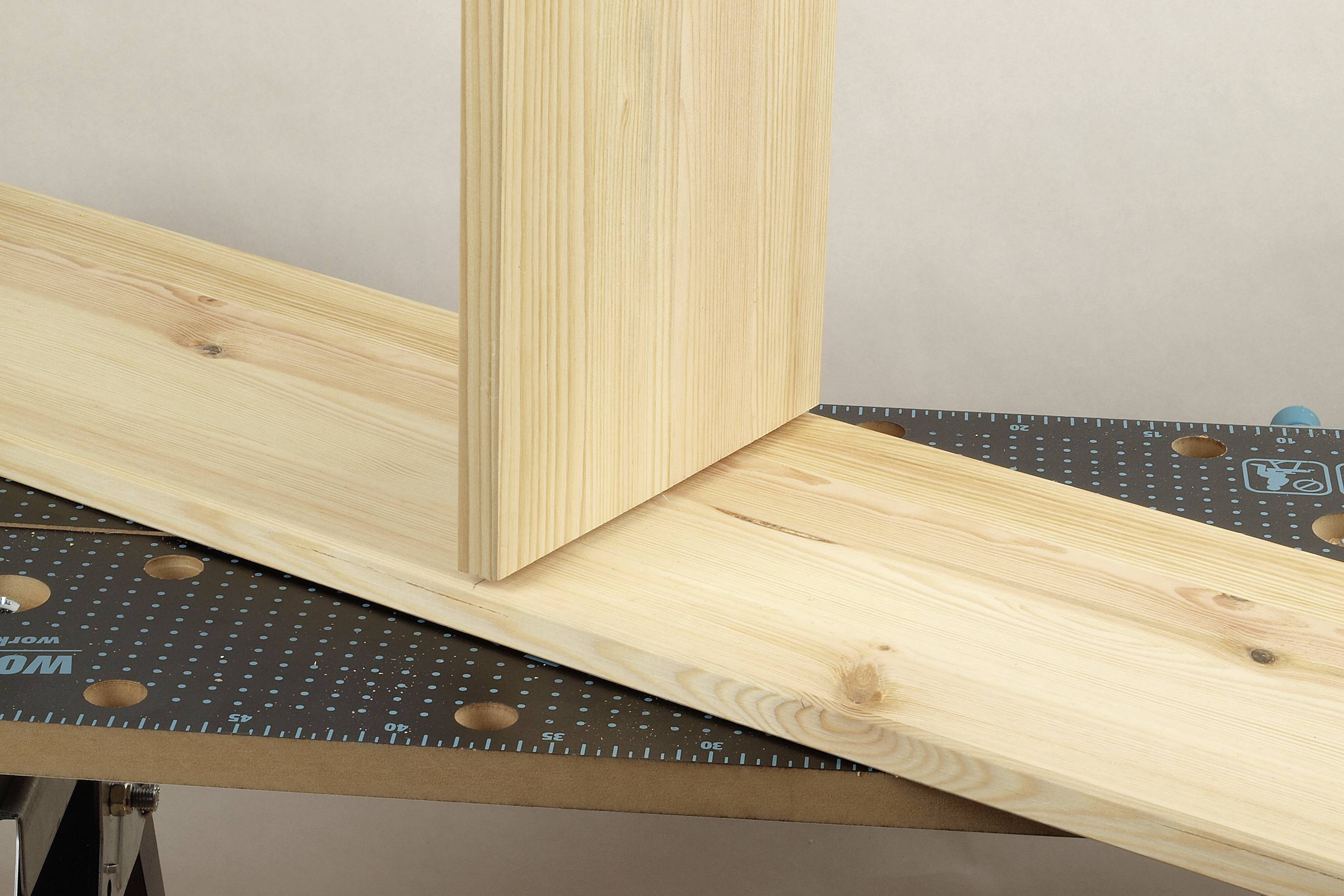 Une planche en bois est positionnée à angle droit sur l'établi, illustrant un travail de menuiserie ou un montage de meuble.