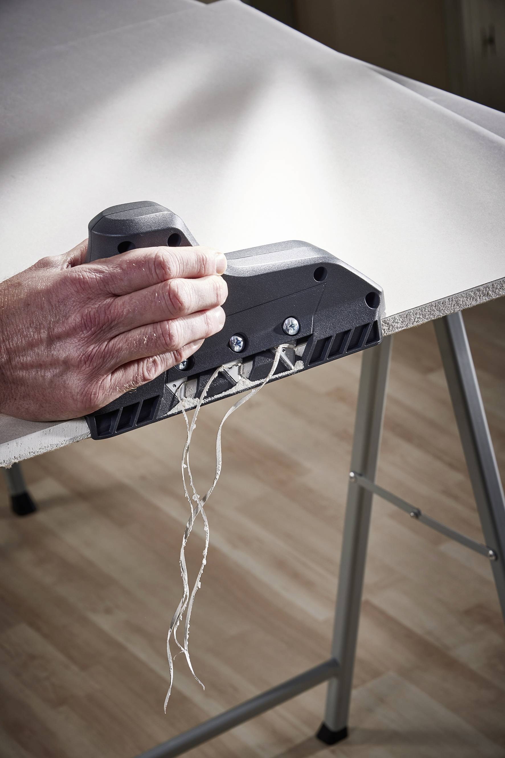 Une main utilise un outil pour lisser les bords d'un grand matériau blanc, tandis que des fils pendent.
