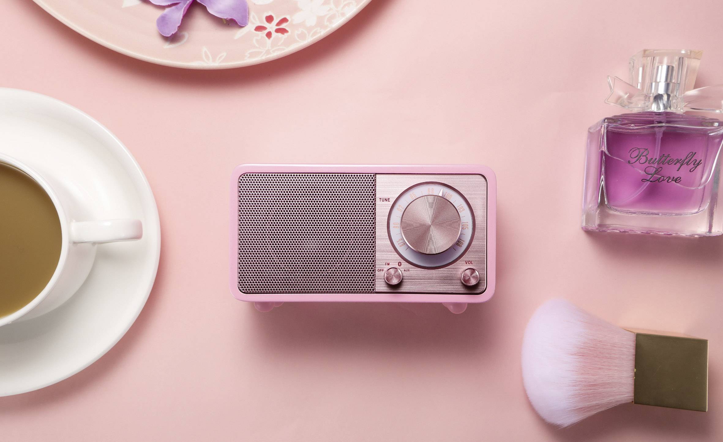 Radio vintage rose sur fond rose, entouré d'une tasse de café, d'un flacon de parfum et d'un pinceau de maquillage.