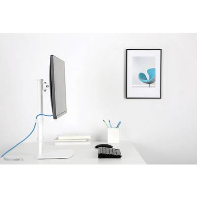 Un espace de travail moderne avec un écran latéralement monté sur une table blanche. À côté se trouvent des livres, des stylos et un clavier. Un tableau représentant une chaise bleue est accroché au mur.
