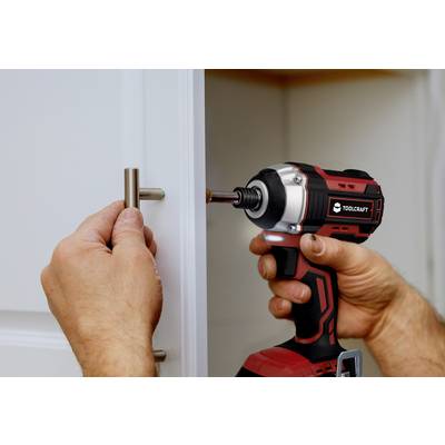 Une personne installe une poignée avec un tournevis sans fil rouge. La poignée est fixée sur une porte d'armoire blanche.