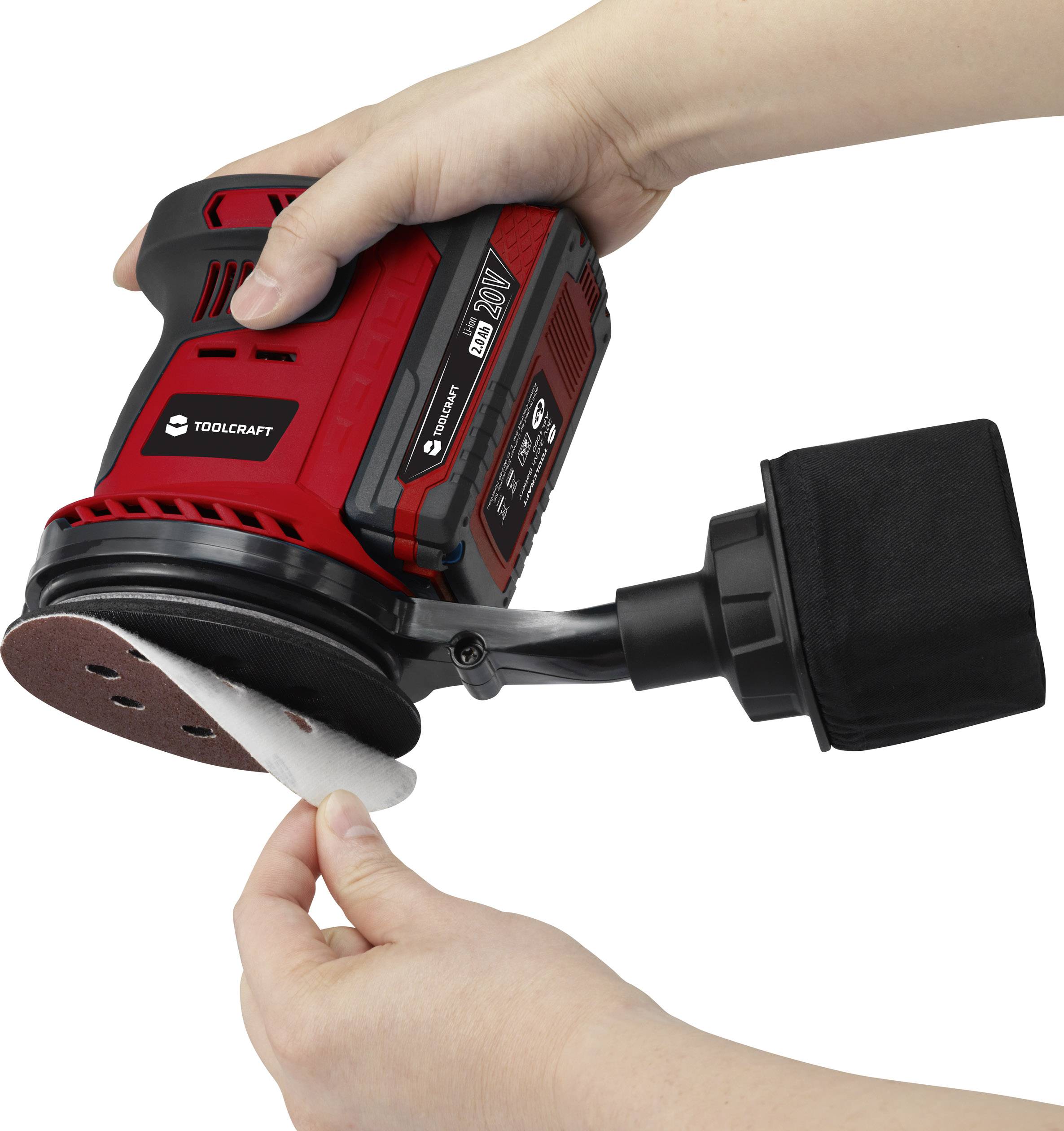 Une personne change le papier de verre sur un appareil de ponçage électrique portable rouge avec un sac à poussière noir.