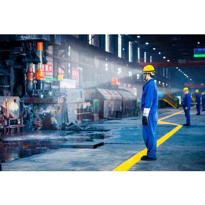 Ouvriers portant des vêtements de protection et des casques, travaillant sur une ligne de production dans un grand hall d'usine. Des machines industrielles sont visibles en arrière-plan.