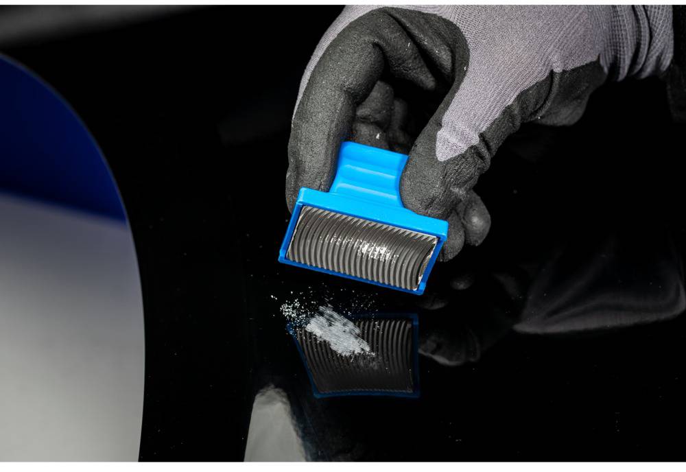 Une main gantée tient un outil bleu au-dessus d'une table noire. Une petite quantité de poudre blanche est répandue sur la surface.