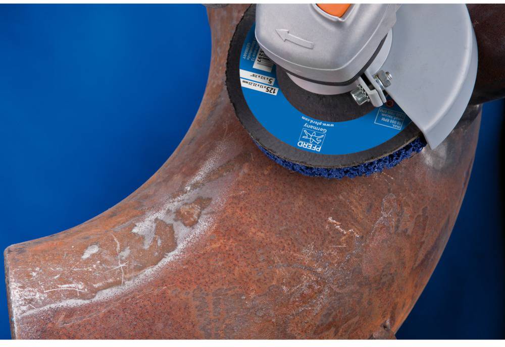 Une meuleuse usine un tuyau rouillé à l'aide d'un disque abrasif. La machine est montrée près du tuyau.