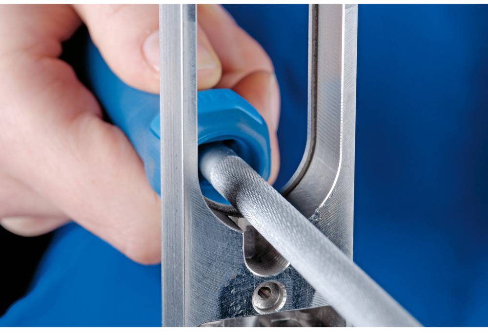 Une main tient un outil bleu qui insère un fil gris dans un appareil métallique.