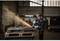 Une personne en équipement de protection meule du métal avec une meuleuse d'angle, des étincelles jaillissent. Atelier industriel en arrière-plan.