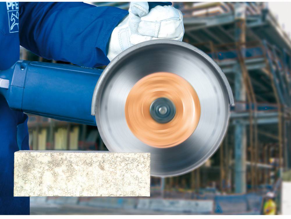 Une personne en tenue de travail coupe une pierre à l'aide d'une scie circulaire rotative. Un chantier de construction est visible en arrière-plan.