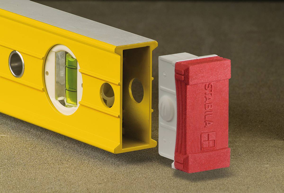 Un niveau à bulle jaune avec des fenêtres de visée posé sur une surface. À côté de lui se trouve un capuchon rouge portant l'inscription 'Stabila'.