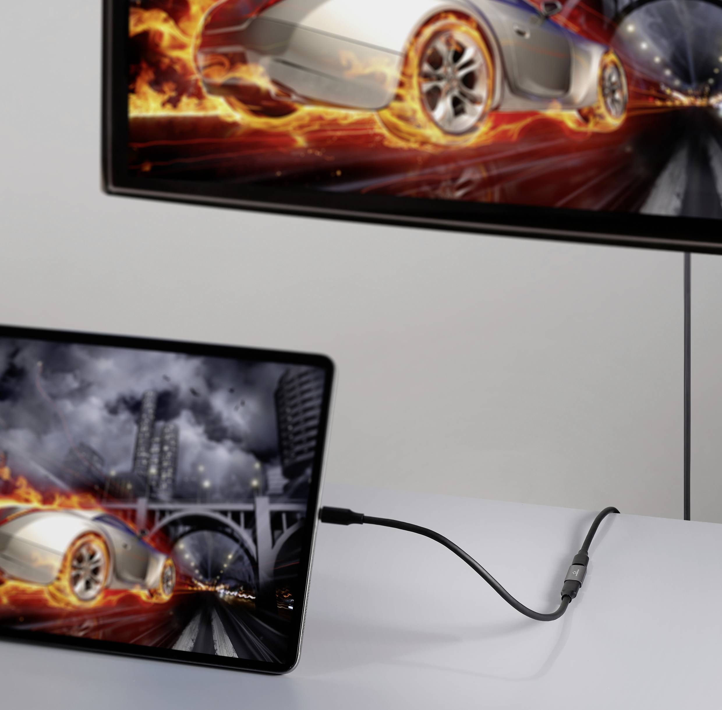 Une tablette affiche l'image d'une voiture avec des effets de flammes. Elle est connectée par un câble à un écran plus grand qui montre la même image.