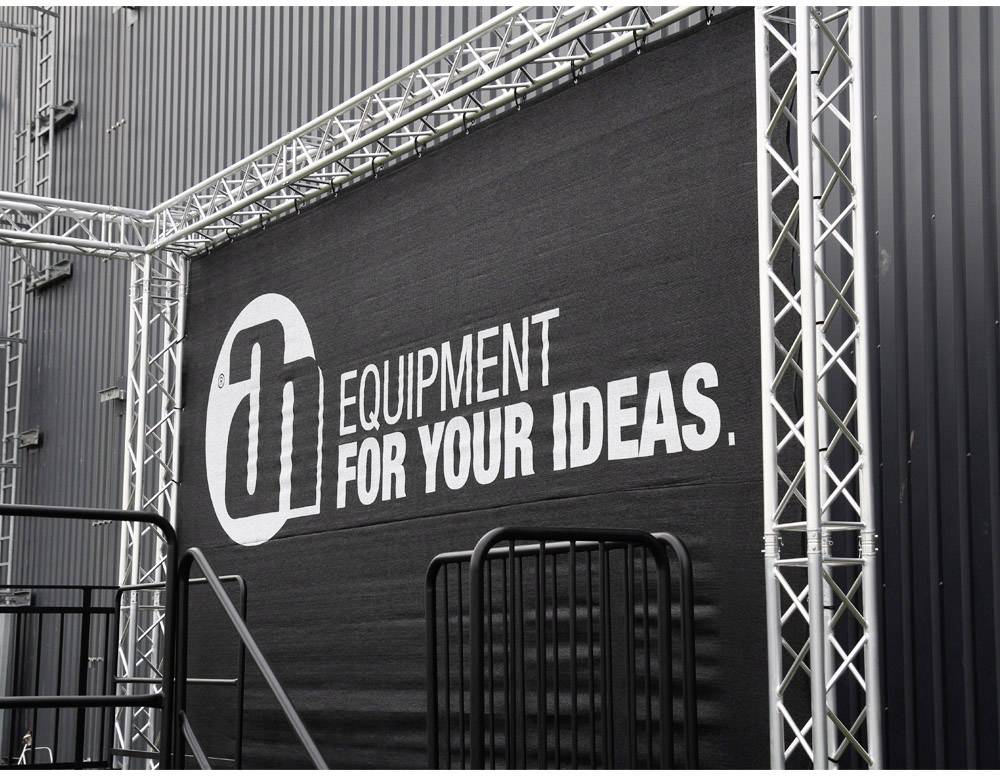 Mur noir avec le texte 'EQUIPMENT FOR YOUR IDEAS' en blanc. Entouré d'un échafaudage argenté.