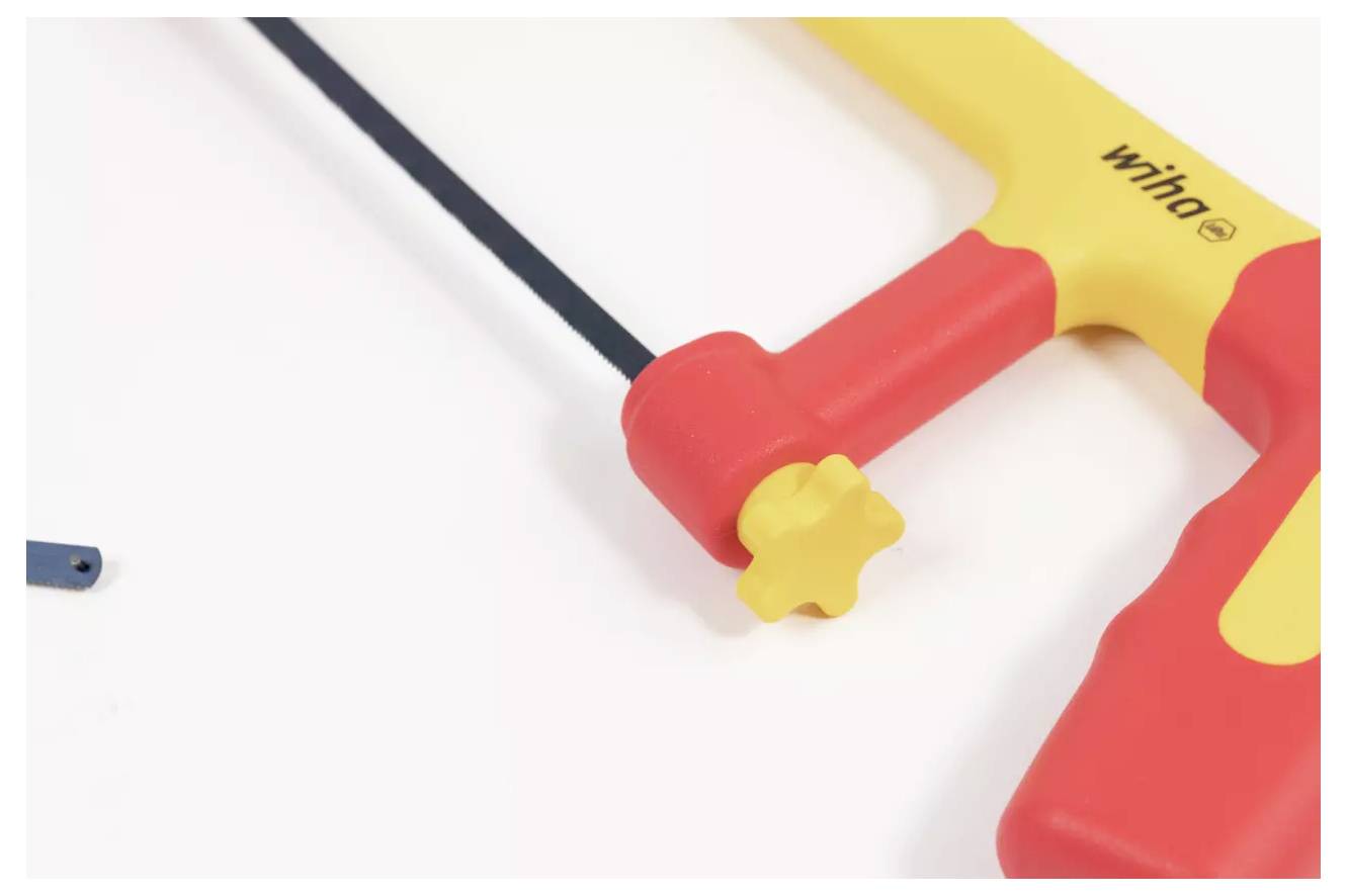 Une scie à main rouge et jaune avec une lame noire, partiellement visible sur une surface blanche, mettant l'accent sur sa poignée et son bouton de tension.