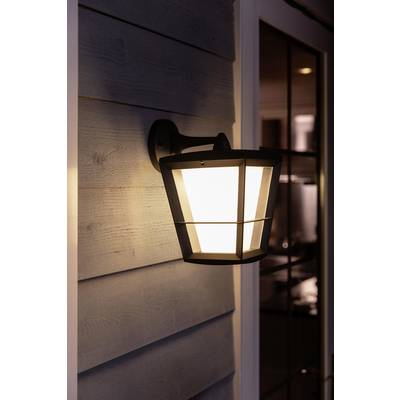 Lampe extérieure éclairant une véranda au crépuscule, fixée à un mur recouvert de lambris, à côté d'une porte vitrée.