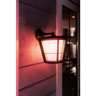 Applique murale éclaire le mur d'une lueur rouge douce. La forme de la lampe est moderne, la fenêtre rectangulaire reflète la lumière, créant une ambiance chaleureuse du soir.