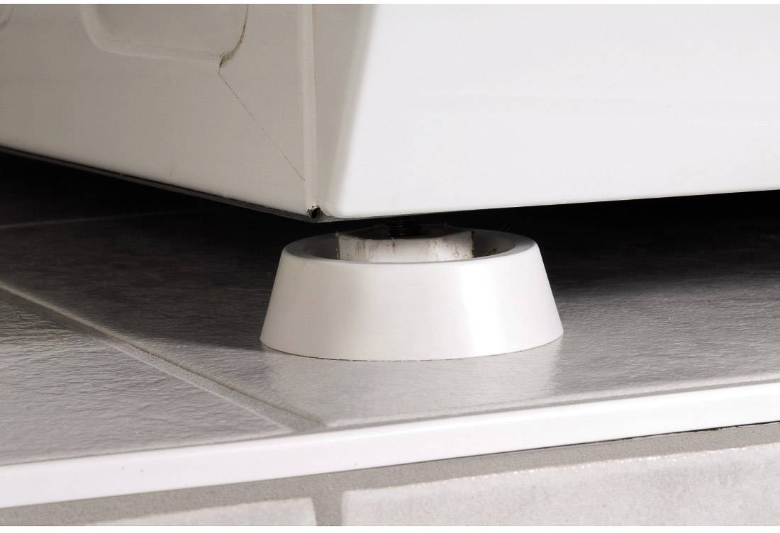 Machine à laver placée sur un cône anti-vibrations blanc sur des carreaux de sol, afin d'atténuer les vibrations et de réduire le bruit.