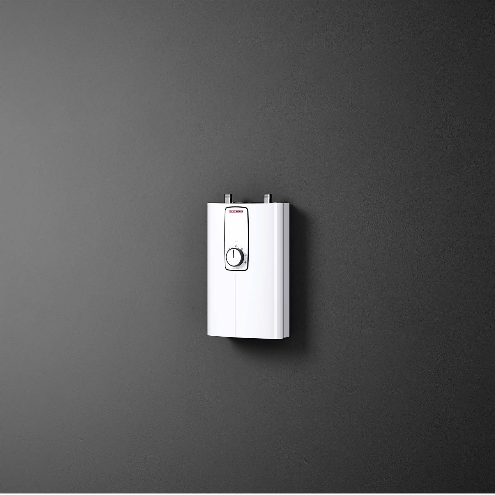 Un chauffe-eau électrique moderne, mural, avec un bouton central rotatif, est situé devant un mur gris.