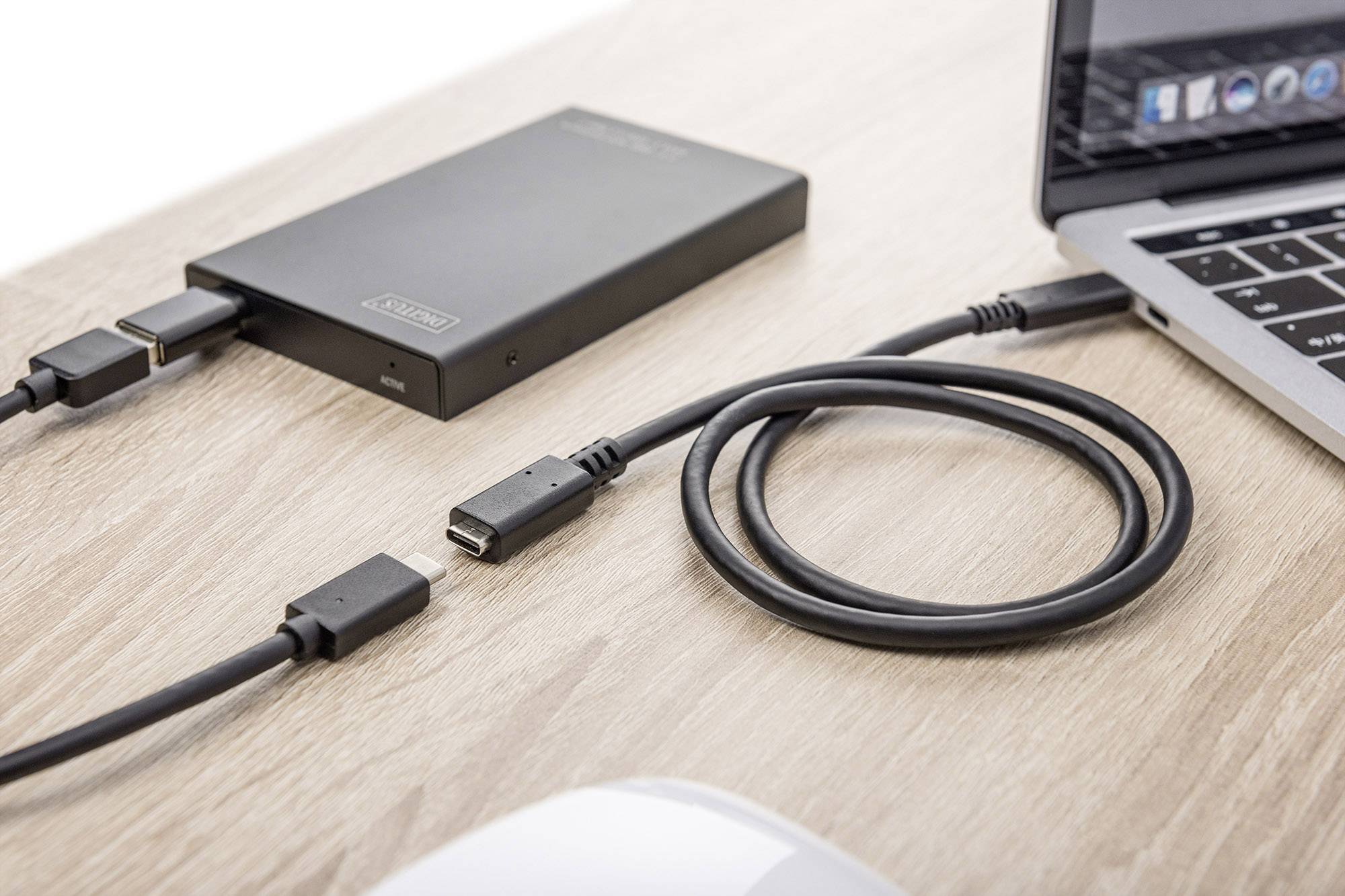 Un ordinateur portable est connecté à un disque dur externe via un câble USB. Les deux appareils sont posés sur une table en bois.