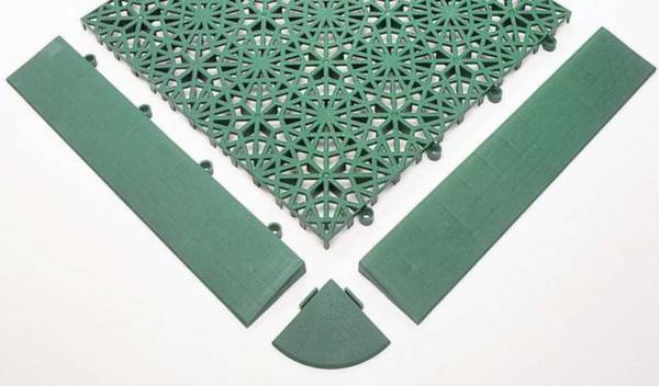 Plaques de plastique vertes avec système d'emboîtement, composées d'un réseau quadrillé et de trois éléments de bordure, sur un fond clair.