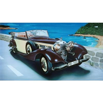 Une voiture décapotable classique roule le long d'une route côtière, avec la mer et une péninsule boisée en arrière-plan.